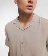 Camisa boxy masculina de viscosa color beige, con mangas cortas, cuello camisero y abotonadura frontal.