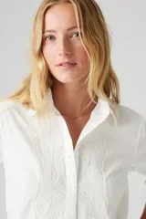 Camisa blanca de manga larga con bordado floral en el frente y detalle de puntilla en los puños.