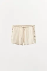 Shorts de tiro alto confeccionados en algodón color crudo, con cintura elástica ajustable con lazada. Presentan bordados y puntilla combinados a tono, con aplicación de abalorios y lentejuelas a contraste.