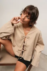 Remera beige de corte oversize con escote en V y mangas largas. Presenta aberturas frontales ajustables con lazos.