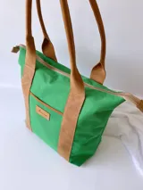 Bolso tipo tote de lona color fucsia con asas de cuero marrón, bolsillo interno y externo.