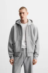 Sudadera negra relaxed fit de algodón compacto con interior en rizo, cuello con capucha ajustable, manga larga, bolsillos frontales tipo canguro, acabados en rib y cierre frontal con cremallera.