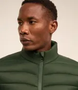 Campera puffer ultraligera color beige, con cuello alto, cierre por cremallera y bolsillos con cremallera. Incluye bolso de almacenamiento.