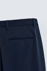 Pantalón de vestir azul marino, de corte slim fit, con bolsillos laterales y traseros. Se ajusta a la cintura con cinturón de cuero marrón.