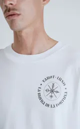 Remera blanca de manga corta con cuello redondo y calce oversize. Presenta una estampa en sublimación inspirada en el tarot, con la imagen de una figura femenina sosteniendo un salvavidas con la frase "Chill Bitch Trust Karma" y el texto "The Wheel of Fortune" en la parte inferior.