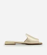 Sandalia plana tipo mule, color dorado metálico, con una tira ancha que cubre la parte delantera del pie y un pequeño tacón cuadrado.