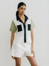 Camisa de manga corta con diseño color block, combinando paneles blancos, verde oliva y detalles en negro (cuello, tapeta de botones y bolsillos de parche).