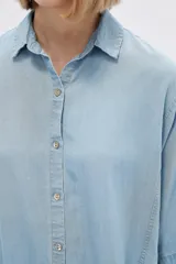 Camisa celeste de manga corta, corte holgado, con cuello camisero y cierre frontal con botones.