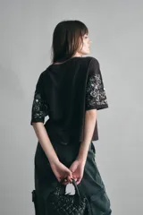 Remera marrón holgada de algodón con escote redondo y mangas al codo. Presenta bordados de canutillos y lentejuelas en las mangas.