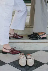 Sueco de cuero negro con cordones, ojales, hebillas y tira trasera regulable con elástico. Tiene taco cuadrado bajo.