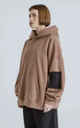 Hoodie marrón de algodón rústico con silueta oversize, capucha forrada, bolsillo tipo canguro y bolsillo en la manga con cierre.