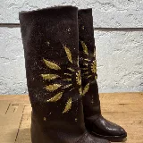 Bota de cuero marrón con bordado dorado en forma de sol.