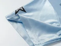 Remera estilo jersey de fútbol o americana, color celeste claro, con paneles de tela satinada y malla microperforada. Presenta cuello en V con ribete blanco, el número "90" grande en el frente con borde negro, y texto en la parte superior que dice "BAEN MADE" y "Madcapsclub".