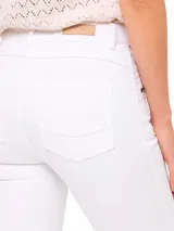 Pantalón de jeans blanco, corte skinny, tiro medio, con bolsillos delanteros con cierre metálico color bronce y ruedo desflecado.