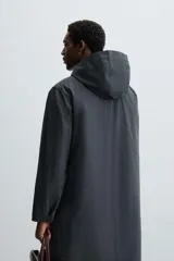 Parka larga color verde oscuro, con capucha desmontable, cuello solapa, bolsillos laterales y cierre frontal con cremallera oculta y botones a presión. Incluye chaleco interior acolchado desmontable.