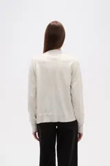 Cardigan de punto color blanco roto con motas oscuras, de manga larga y escote en V con cierre de botones frontales.