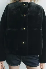 Chaqueta corta de cuello redondo y manga larga en tejido de pelo sintético color negro. Cierre frontal con botones metálicos dorados y bolsillos de plastrón. Colección Zara Woman.