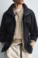 Parka azul marino de tejido técnico, corte relaxed fit, cuello alto ajustable con cordón, manga larga con puños abotonados, cierre frontal con cremallera oculta y solapa con botones a presión, cintura ajustable con cordón interior y bolsillos frontales multifunción de plastrón.