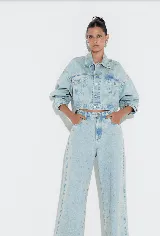 Campera cropped de denim celeste con tachas plateadas formando el logo de la marca.