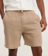 Bermuda de hombre color blanco crudo, confeccionada en algodón texturizado. Presenta un corte comfort, cintura elástica con lazo ajustable y bolsillos laterales.