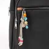 Mochila negra con bolsillo frontal con cierre, manija superior y tiras traseras regulables. Incluye llavero decorativo con cuentas de colores.