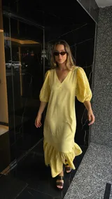 Vestido largo color amarillo pálido, con escote en V, mangas cortas abullonadas con detalle de calado y ruedo con volantes y calado.