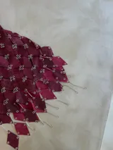 Vestido corto de diseño exclusivo, color bordó, confeccionado artesanalmente con piezas de material texturado (efecto cocodrilo) unidas con argollas metálicas. Presenta tirantes ajustables y un ruedo con terminaciones en forma de rombos colgantes con detalles metálicos.