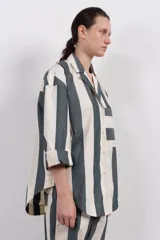 Camisa con corte estilo blazer, a rayas verticales color gris y blanco, con cuello clásico, cierre frontal con botones, bolsillo de parche en el pecho y mangas largas amplias.