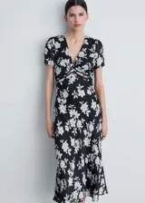Vestido midi de mangas cortas con estampado floral blanco sobre fondo negro. Tiene escote en V con detalle de frunce en el centro del busto y falda con corte al bies.