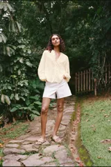 Blusa color crema de escote pico con volantes y manga larga. Detalle de jaretas y entredoses a tono. Cierre frontal con botones forrados a tono.