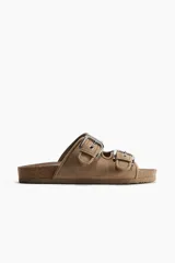 Sandalias planas color beige de gamuza sintética, con dos tiras anchas ajustables mediante hebillas metálicas plateadas.