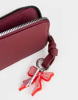 Monedero negro de cuerina con cierre circundante y charm colgante de moño rojo y torre Eiffel plateada.
