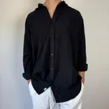 Camisa negra de lino con corte oversize, cuello clásico y mangas largas con puños abotonados.