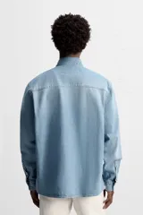 Camisa celeste de denim de algodón, corte relaxed fit, con cuello solapa, manga larga con puños abotonados, dos bolsillos de parche con solapa en el pecho, efecto lavado y cierre frontal abotonado.