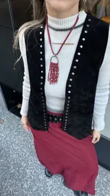 Chaleco negro de cuero descarne con terminación en picos y tachas metálicas.