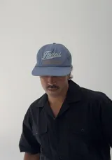 Gorro tipo jockey color azul, con visera curva y bordado frontal que dice "Faded" en blanco y "Sunset Flower Faded Sense Again" en naranja.