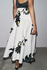 Falda midi de tiro alto confeccionada en hilatura de algodón color blanco con estampado floral en negro y amarillo. Tiene cierre con cremallera oculta en la costura y detalle de botones en la cintura.