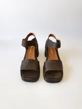 Sandalias de cuero color chocolate, con tira ancha sobre los dedos, pulsera al tobillo con hebilla metálica y taco cuadrado de 6 cm.