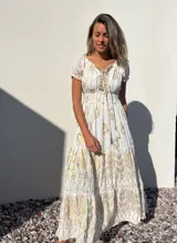 Vestido largo blanco con estampado dorado, escote en V con cordones y mangas cortas abullonadas.