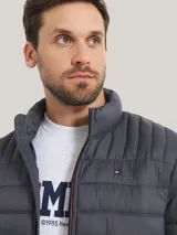 Chaqueta acolchada gris de poliamida con cuello alto, cierre de cremallera, dos bolsillos delanteros con cremallera y logo de Tommy Hilfiger bordado en el pecho.