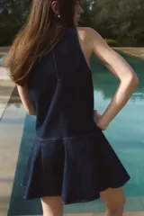 Vestido corto sin mangas en denim azul, con escote redondo y cierre oculto en la espalda. Costura visible en la cadera y pollera acampanada con nesgas para dar vuelo.