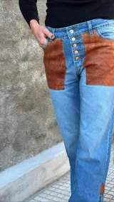 Pantalón de jean con apliques de cuero marrón en los bolsillos delanteros y en el ruedo.
