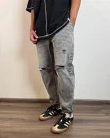 Pantalón jean gris con efecto lavado, corte slouchy, tiro alto, roturas en las rodillas y largo al tobillo.