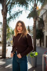 Buzo gris de punto con cuello redondo, mangas largas abullonadas y cierre frontal asimétrico.