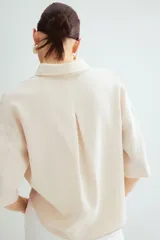 Camisa color crema en tejido liviano de lino y viscosa con cuello, botones adelante y pliegue de caja invertido en la espalda. Modelo de corte holgado con hombros marcadamente caídos, mangas al codo y bajo levemente redondeado.