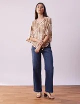 Blusa de crepe color beige con estampado de hojas blancas, cuello redondo con escote en V y lazo de ajuste, mangas 3/4 con tajo.