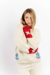 Sweater tejido a mano en lana merino color crudo, con cuello y puños en rojo. Presenta un diseño con motivos de un cowboy y estrellas.