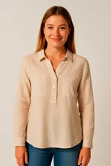 Blusa color beige claro, de corte holgado, con cuello camisero, escote en V y cierre parcial con botones. Presenta mangas largas con puños abotonados y dos bolsillos de parche en el pecho.