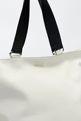 Bolso blanco de símil cuero con terminación suave. Tiene asas anchas de cinta negra y un bolsillo frontal con solapa.