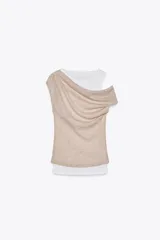 Camiseta blanca de cuello redondo y sisa, con superposición de tejido beige drapeado en un hombro.